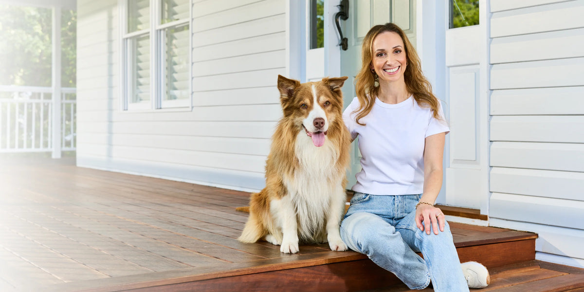 A smiling woman sitting on a verandah step beside a red and white dog